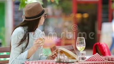 在户外咖啡厅用智能<strong>手机端</strong>着一杯白葡萄酒的年轻女孩。走进去坐着的美女